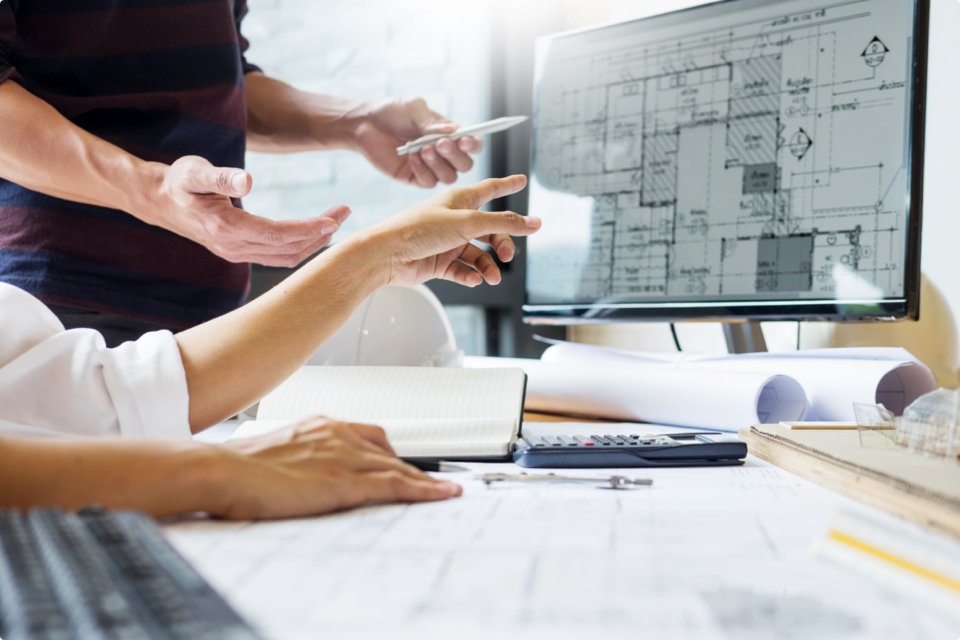 Two people pointing at on floor plan on a desktop
