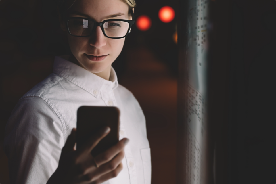 Woman with glasses looking at phone outside at night